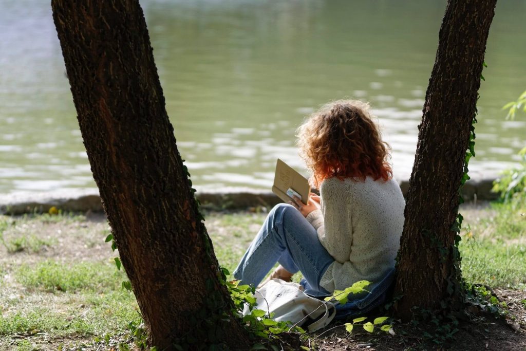 Woman reading book under tree by a stream