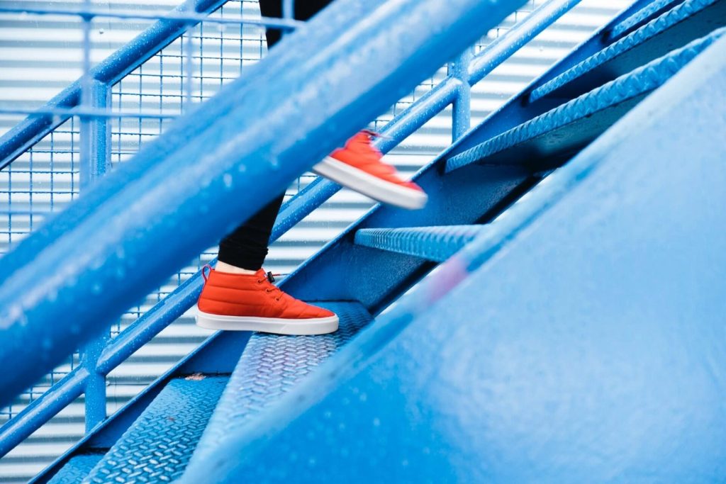 Person with red sneakers walking up blue stairs