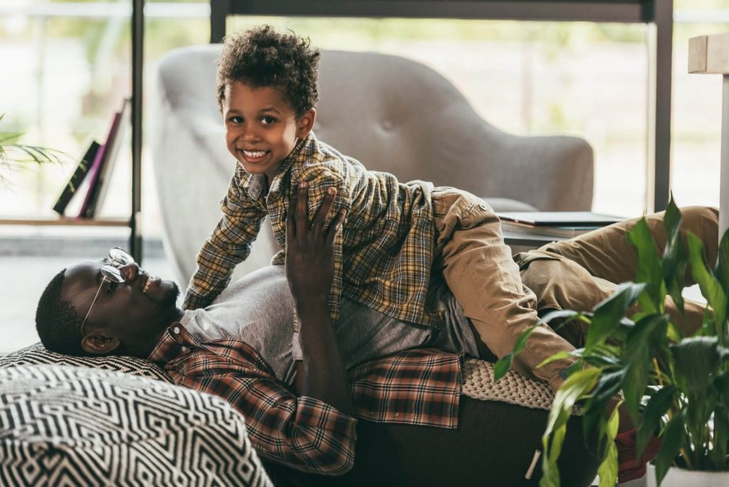 African American man playing with his son on couch